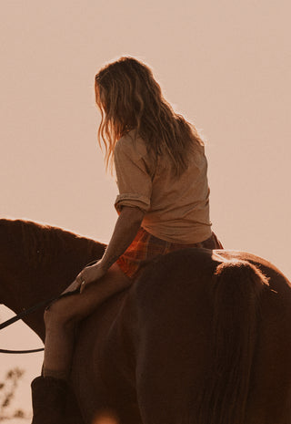 A woman with long light brown hair sits on a horse